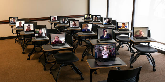 Opened laptops on a desks in a classroom with images of students on each screen
