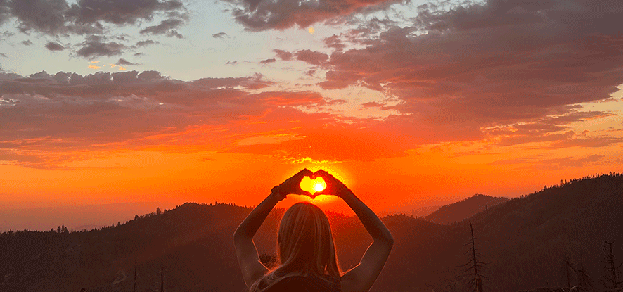 Student making a heart sign above the sunset