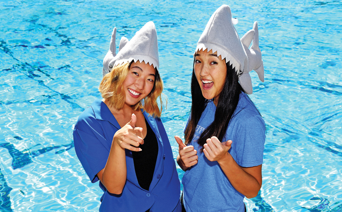 Two female students near pool in shark hats