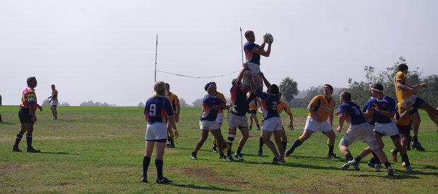 Club Rugby players playing a match on Alumni Park; students raise one player holding the ball