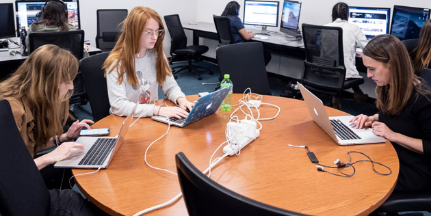 Students working on their laptops sitting at a circular desk in Newswaves 32 office